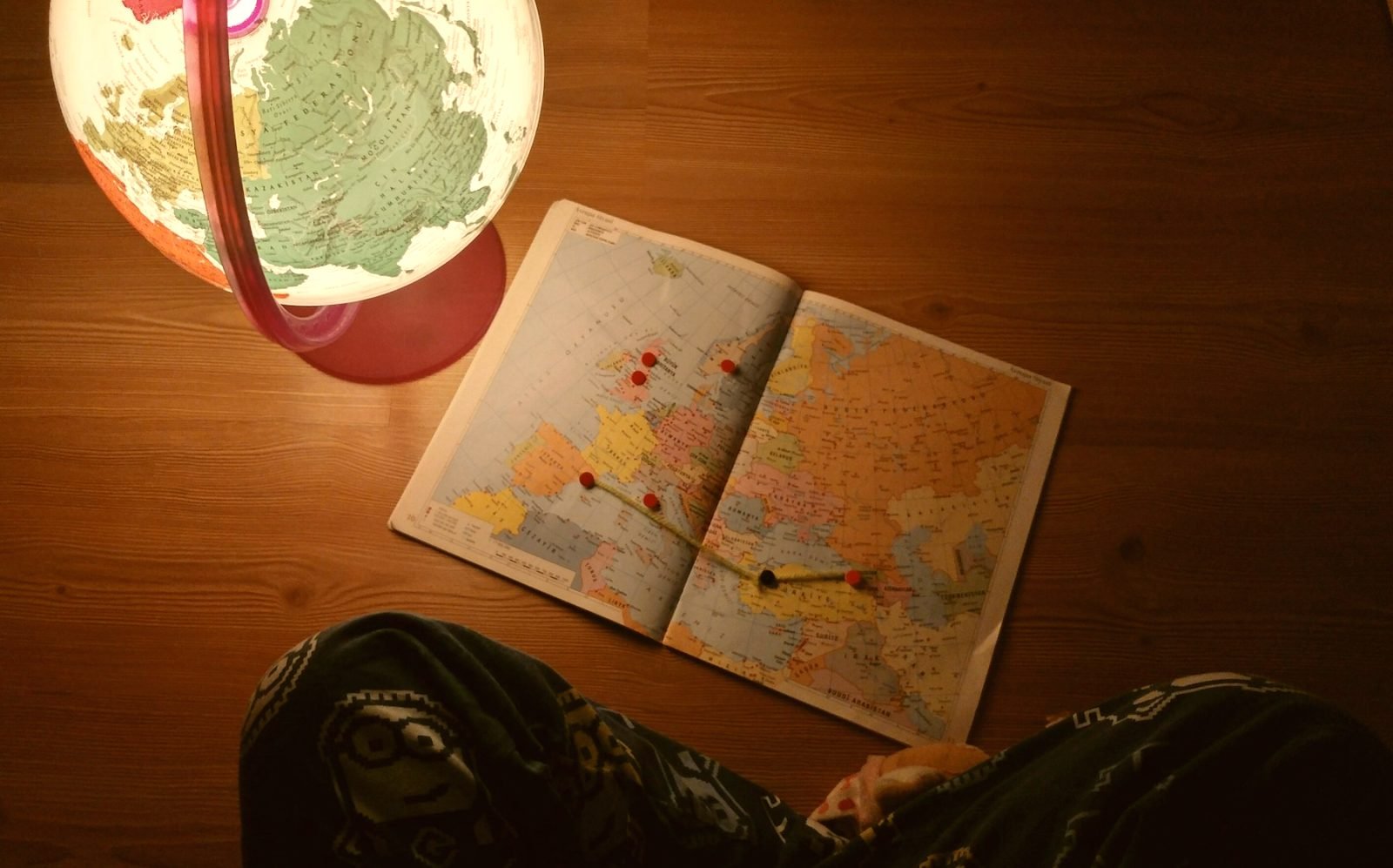 An open atlas with pins marking a route across Europe, beside a globe