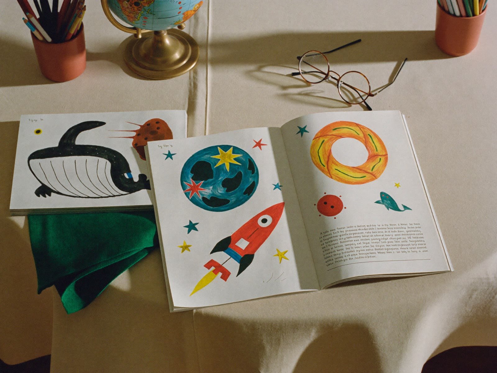 An illustrated children's magazine open on a table with a globe and pencils. Replaces the Bible.